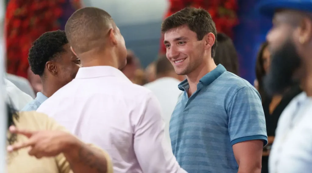 Two men are having a conversation at a social event, with other people mingling in the background.