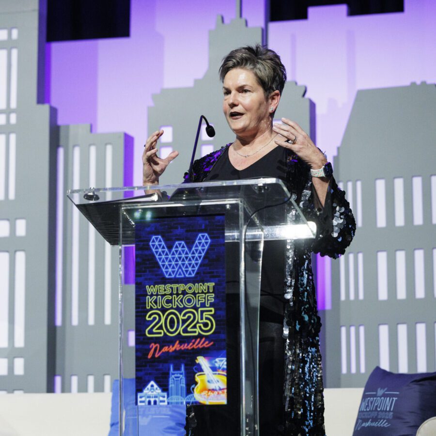 A woman speaks at a podium labeled "WestPoint Kickoff 2025 Nashville" on a stage with cityscape-themed decorations in the background.