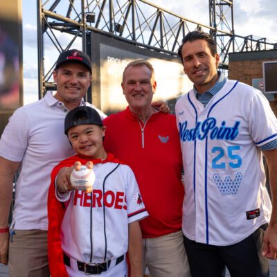 Four people, including a young boy in a baseball uniform holding a ball, stand together smiling on a stadium concourse.