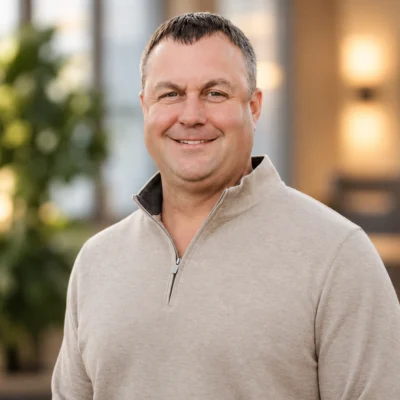 A middle-aged man smiling and wearing a tan quarter-zip sweater.