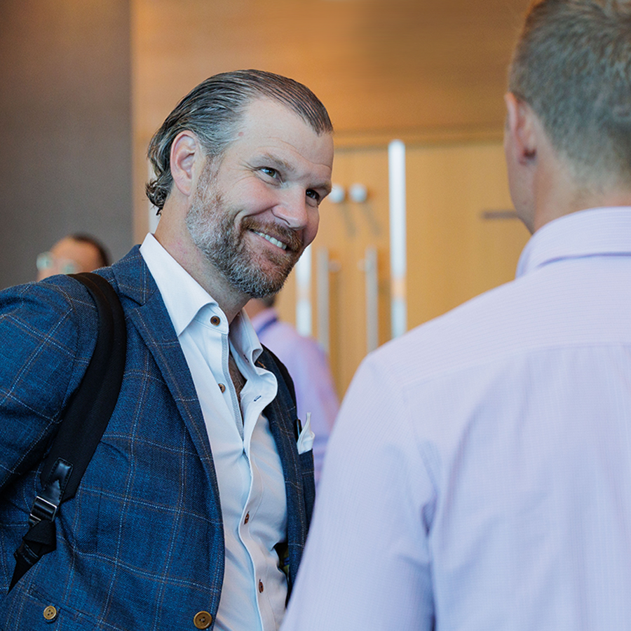 Middle-aged man wearing button up shirt and blazer smiling at person in the foreground.