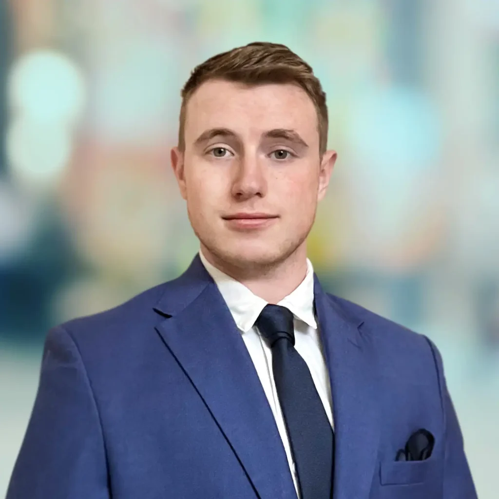 A man in a blue suit, white shirt, and dark tie poses against a blurred background.