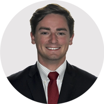 A man in a suit and red tie smiles at the camera against a plain light background.