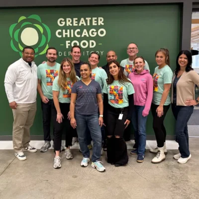A group of eleven people pose together in front of a Greater Chicago Food Depository sign inside a building.