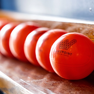 A row of orange balls with a logo and text reading "Westpoint Financial Group" printed on them, placed on a wooden surface.