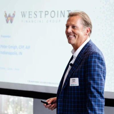 A man in a blue checked suit stands holding a remote, smiling, in front of a projection screen displaying "Westpoint Financial Group.