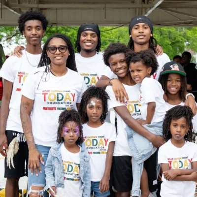 A group of children and young adults wearing matching “Today Foundation” shirts pose together and smile at an outdoor event.