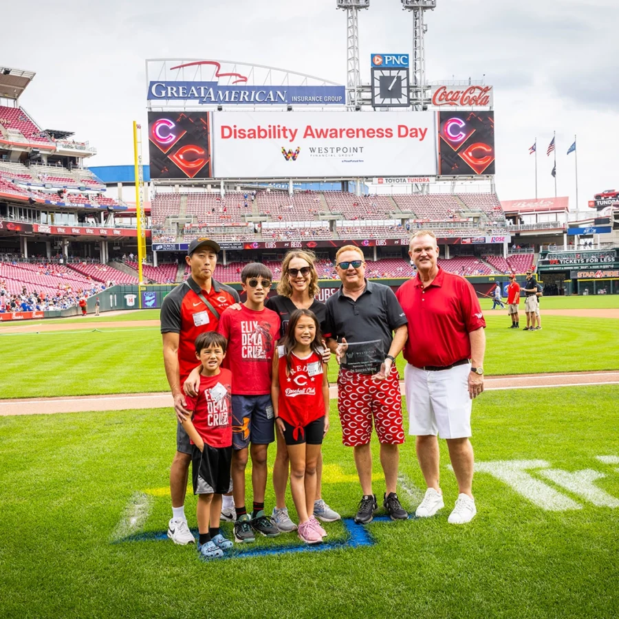 A group of people stands on a baseball field with “Disability Awareness Day” displayed on the stadium screen in the background.