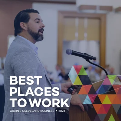 A man speaks at a podium during an event. The text reads, “Best Places to Work, Crain’s Cleveland Business, 2026.” Geometric shapes overlay the lower right corner.